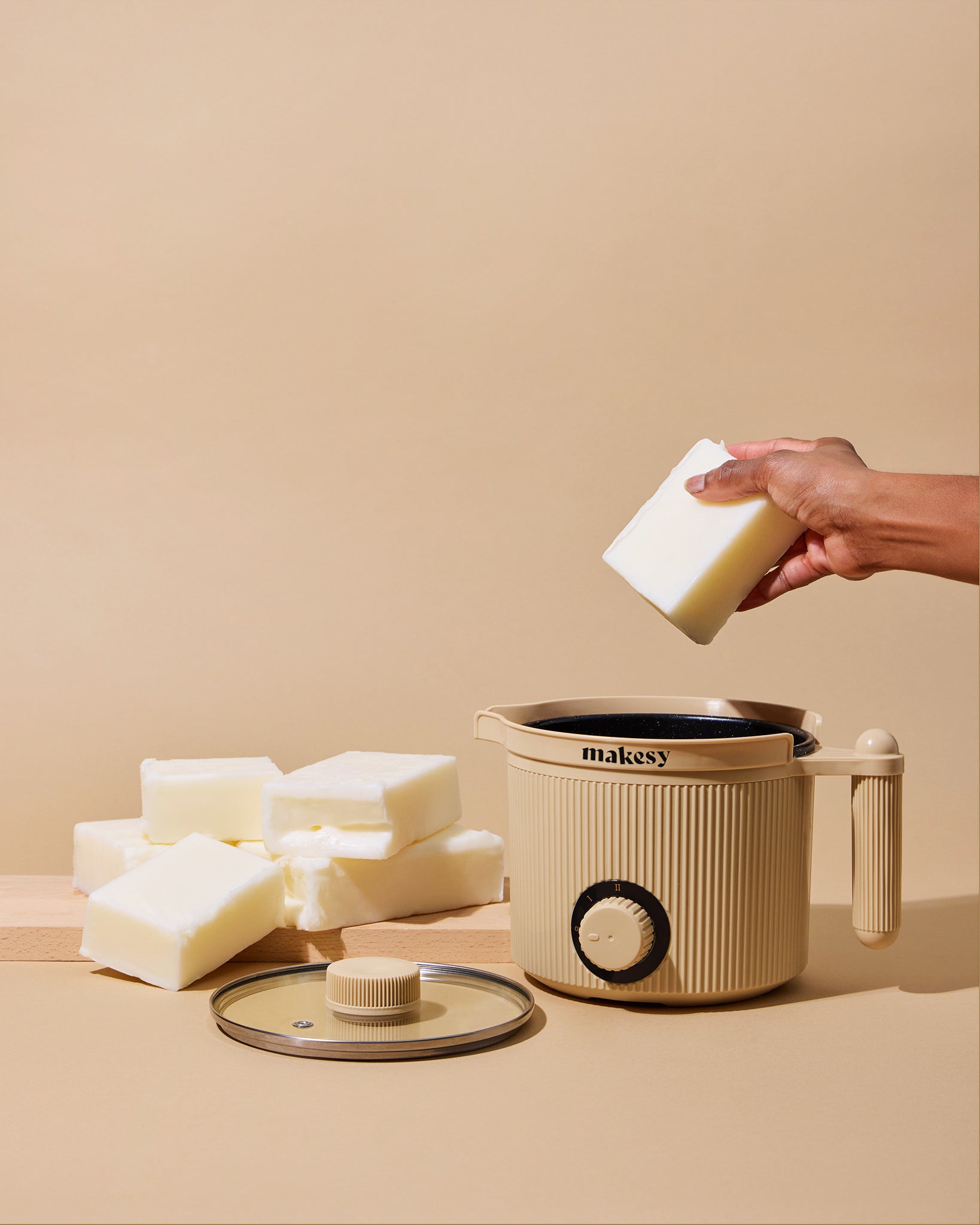 Hand holding a bar of soap above a makesy container on a beige background