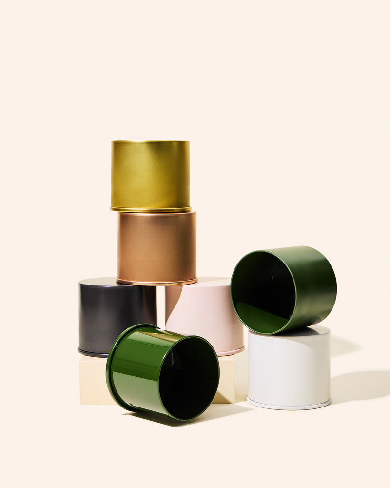 A set of six metallic and glossy cylindrical cups or candle holders in various colors, stacked and arranged on a light cream background.