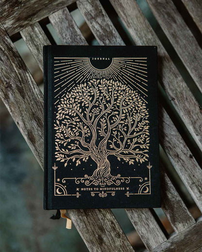 Black notebook with gold tree design on a wooden surface