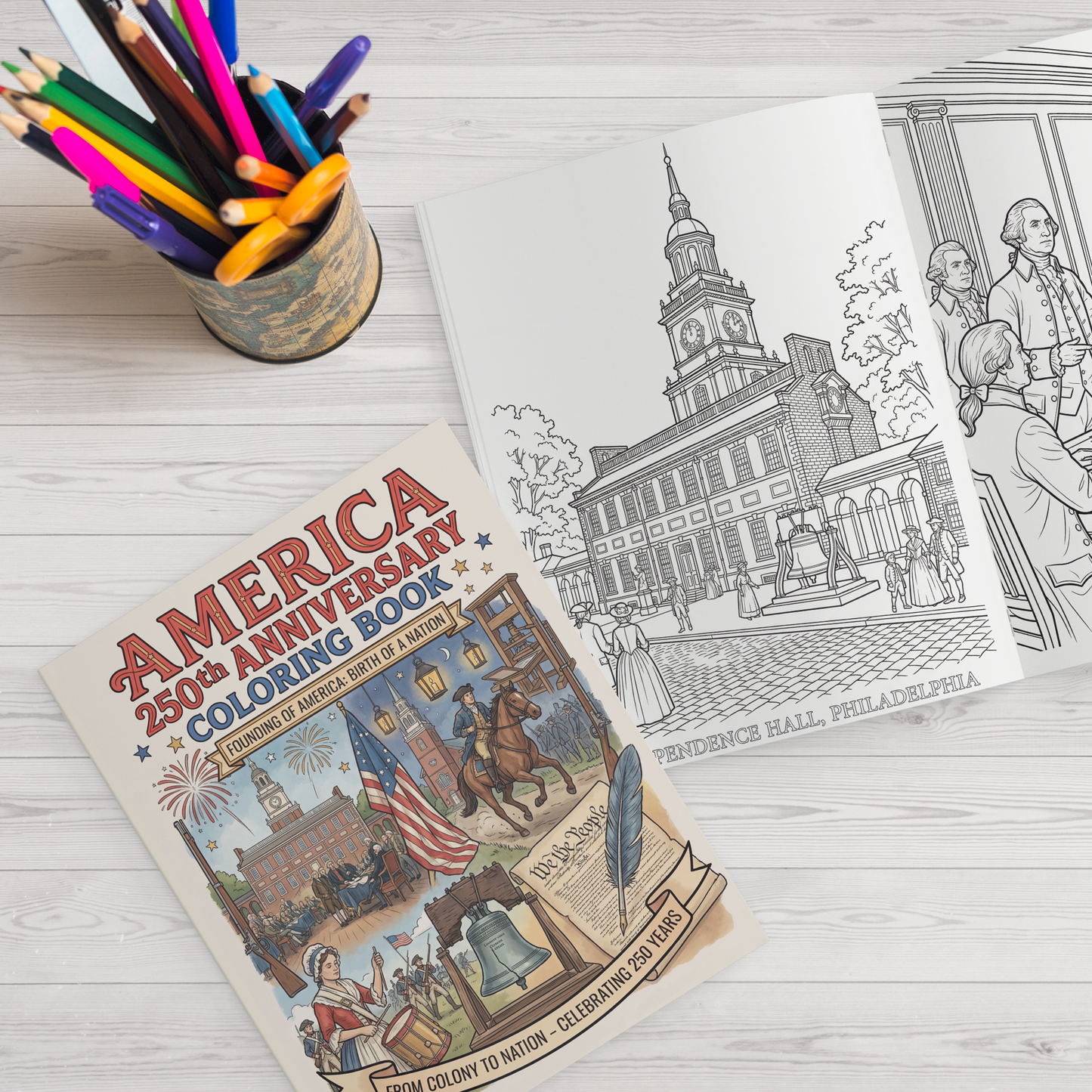Coloring book titled 'America 250th Anniversary' with coloring pages of Independence Hall and people, on a wooden surface with colored pencils.