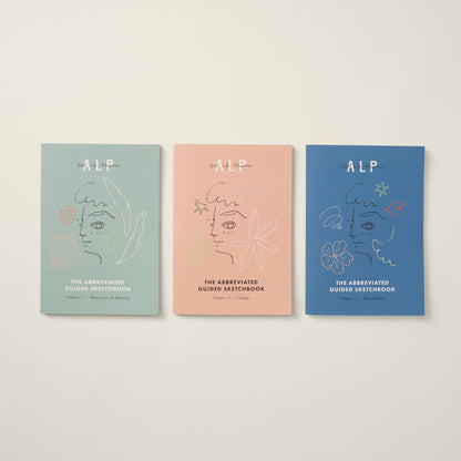 Three 'ALP' guided sketchbooks in different colors on a beige background