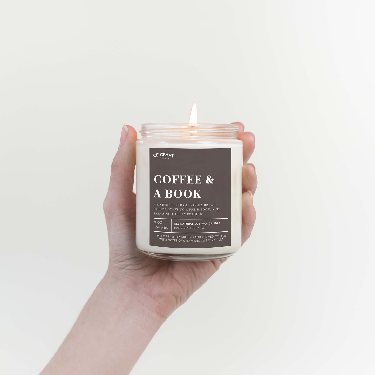 Hand holding a candle labeled 'Coffee & A Book' against a plain background