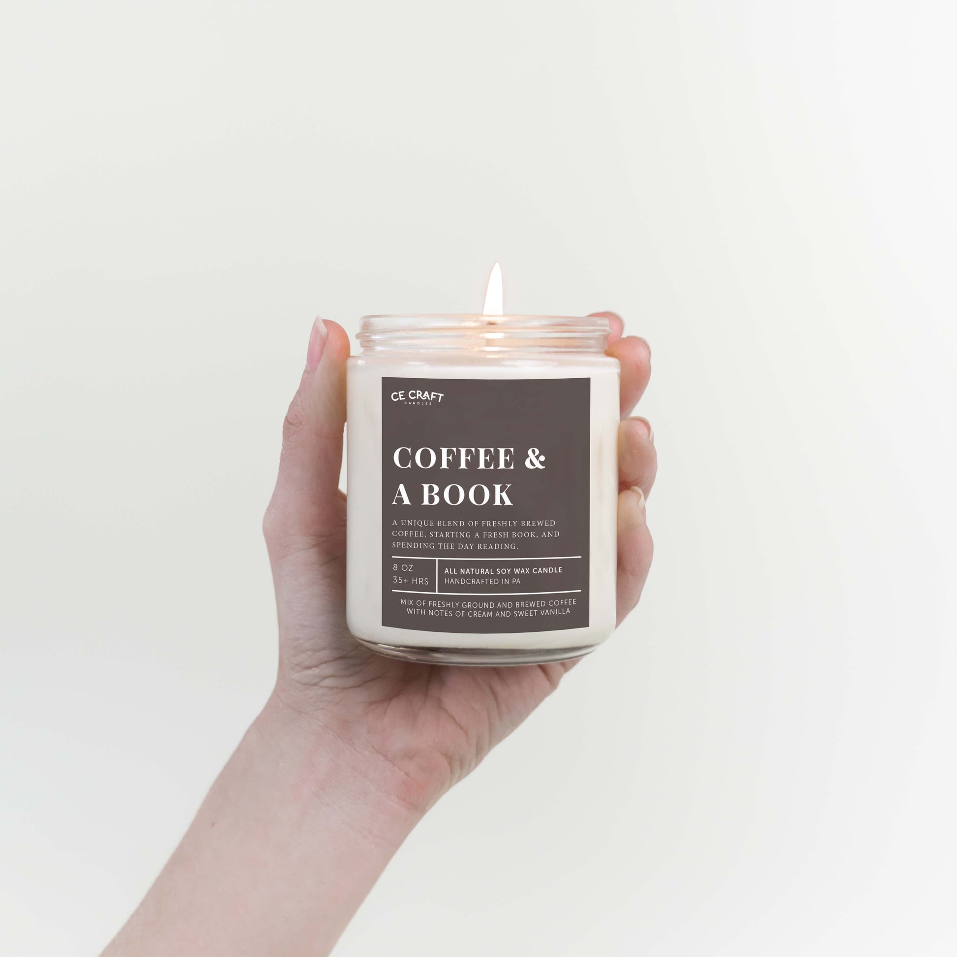 Hand holding a candle labeled 'Coffee & A Book' against a plain background