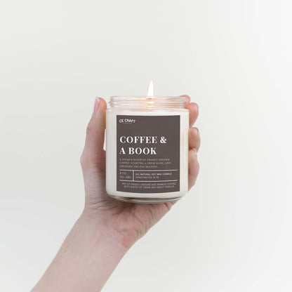 Hand holding a candle labeled 'Coffee & A Book' against a plain background