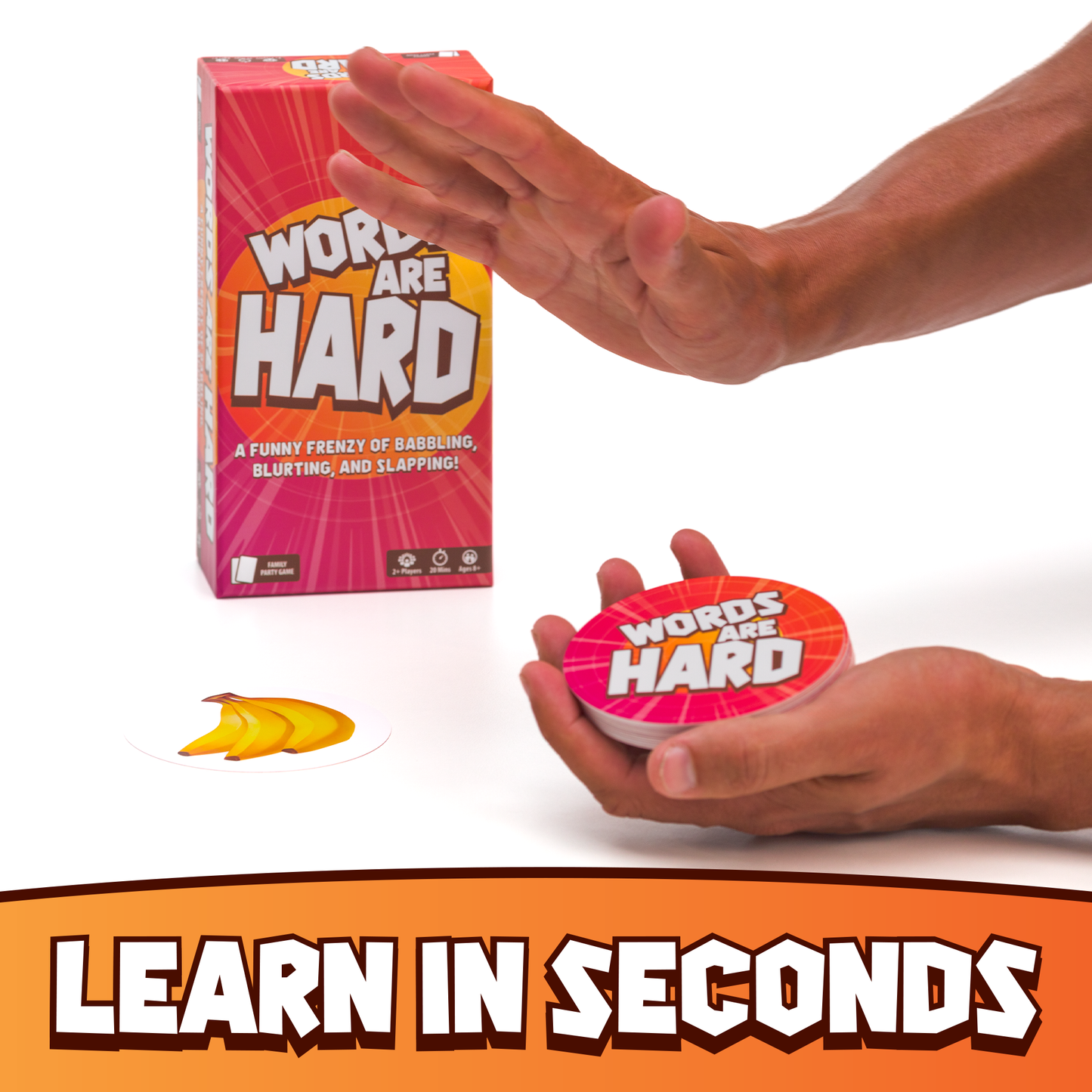Hand holding a 'Words Are Hard' game piece with packaging in the background on a white background.